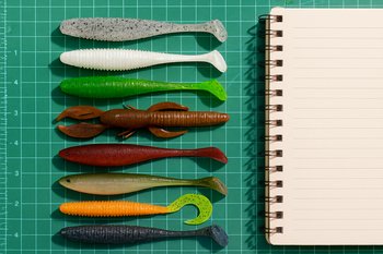 Несколько мягких приманок разложены на коврике рядом с блокнотом